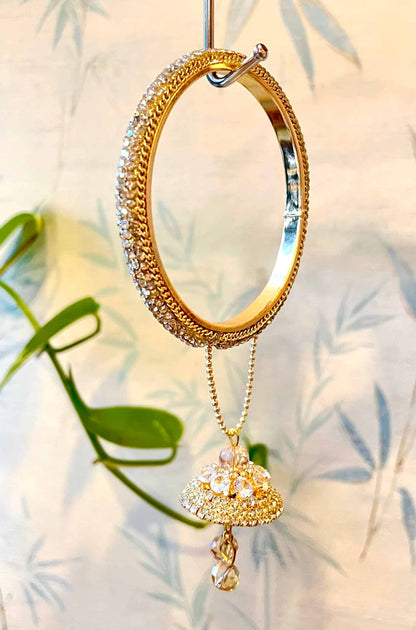 Golden bangle with intricate design and hanging pendant against a light background